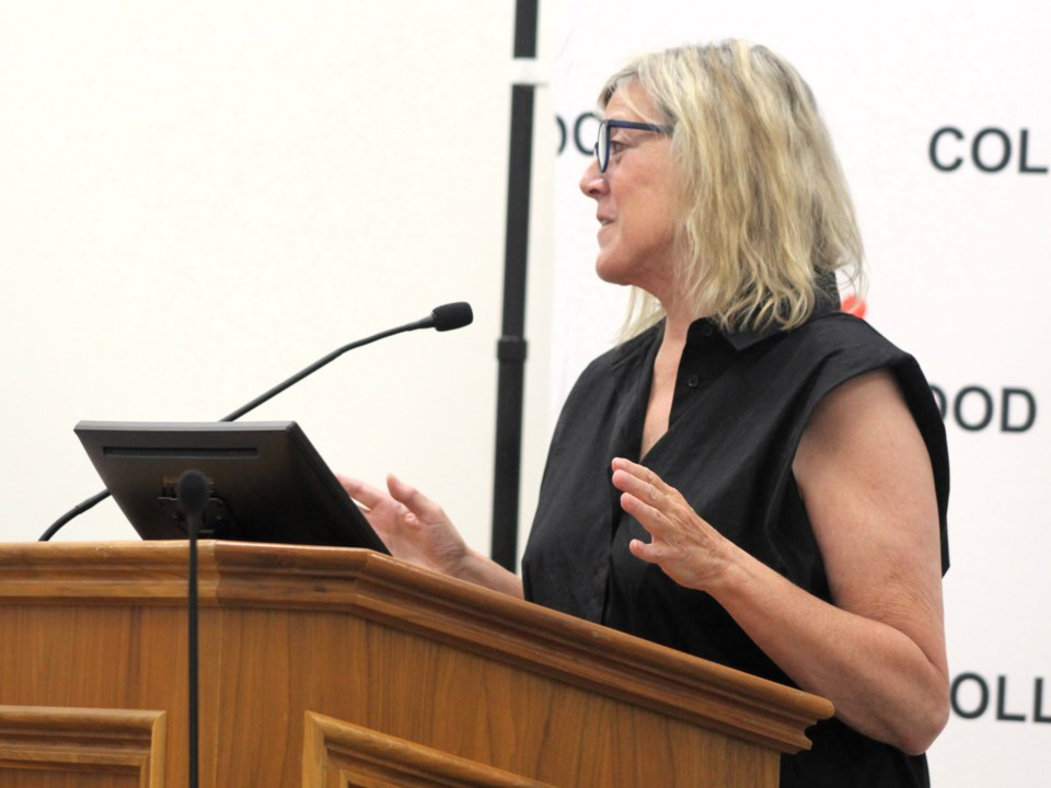 Woman wearing a black shirt stands at a podium speaking into a microphone