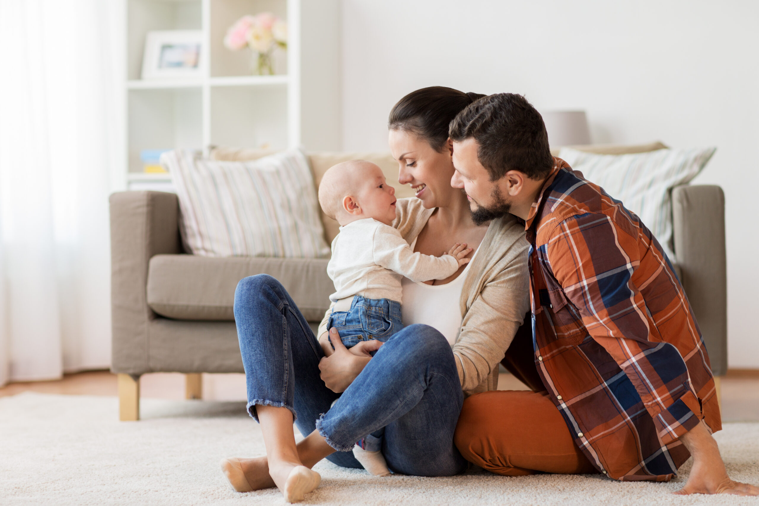 Parents hold baby, sitting on the floor in front of a beige sofa - highlighting CNPH family stories
