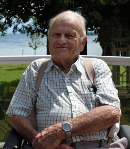 Portrait of Ray Smith, sitting outdoors with trees and the lake in the background